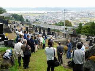 写真　諏訪湖を望む顕彰碑の横で三澤事務局長の挨拶を聞く大勢の参加者